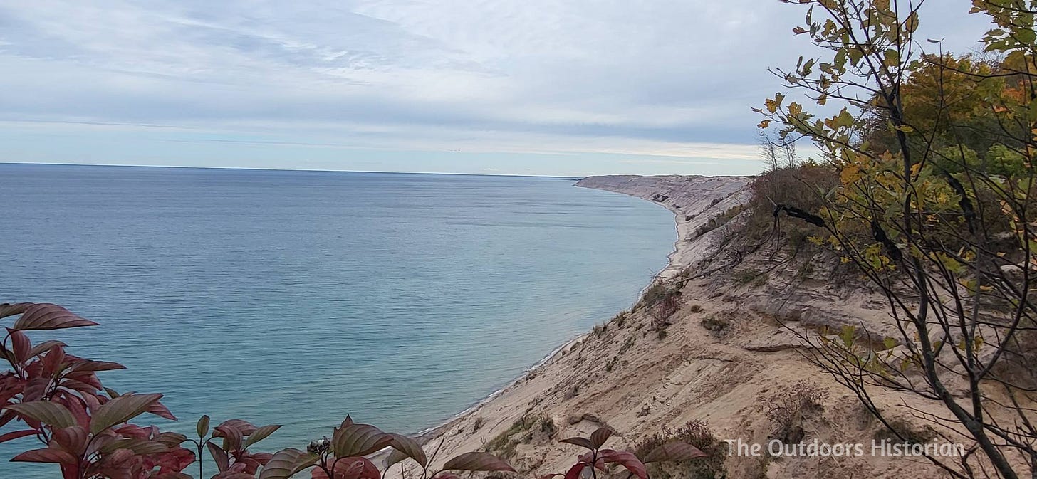A steep sand dune that is several hundred feet tall stretches along Lake Superior as far as the can see.