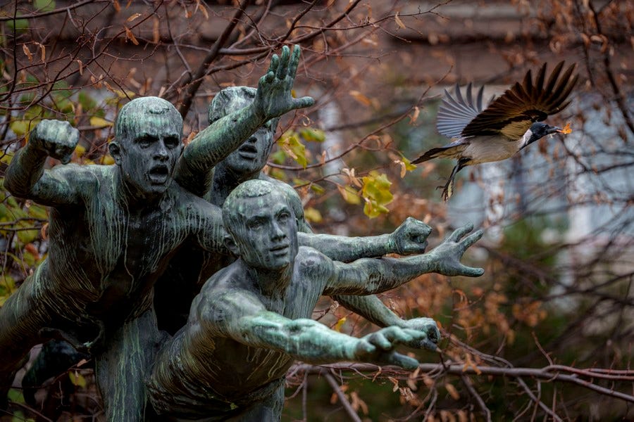 A bird flies past a statue of three men reaching forward, making it appear as if the bird is escaping the men. A bird flies past a statue of three men reaching forward, making it appear as if the bird is escaping the men.