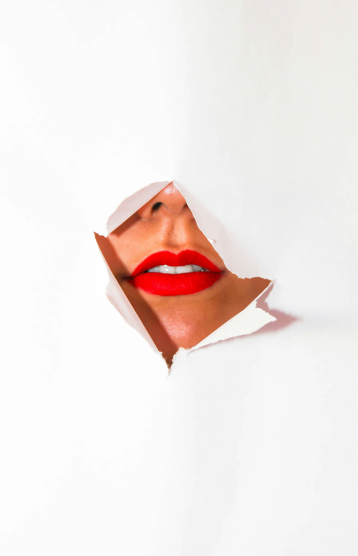 A woman in red lipstick breaks through a sheet of white paper