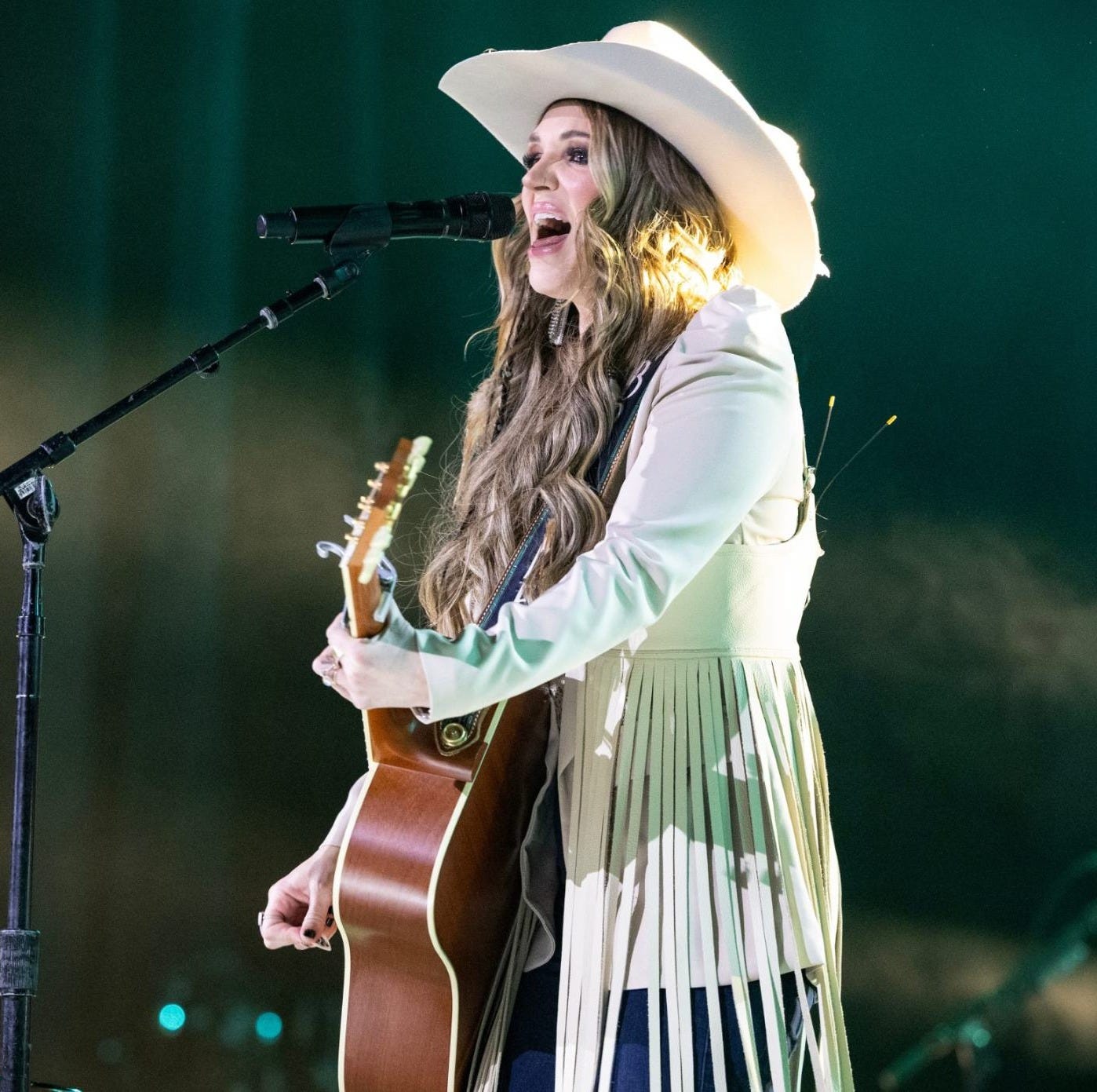 Britnee stands on a stage performing near a microphone while playing guitar