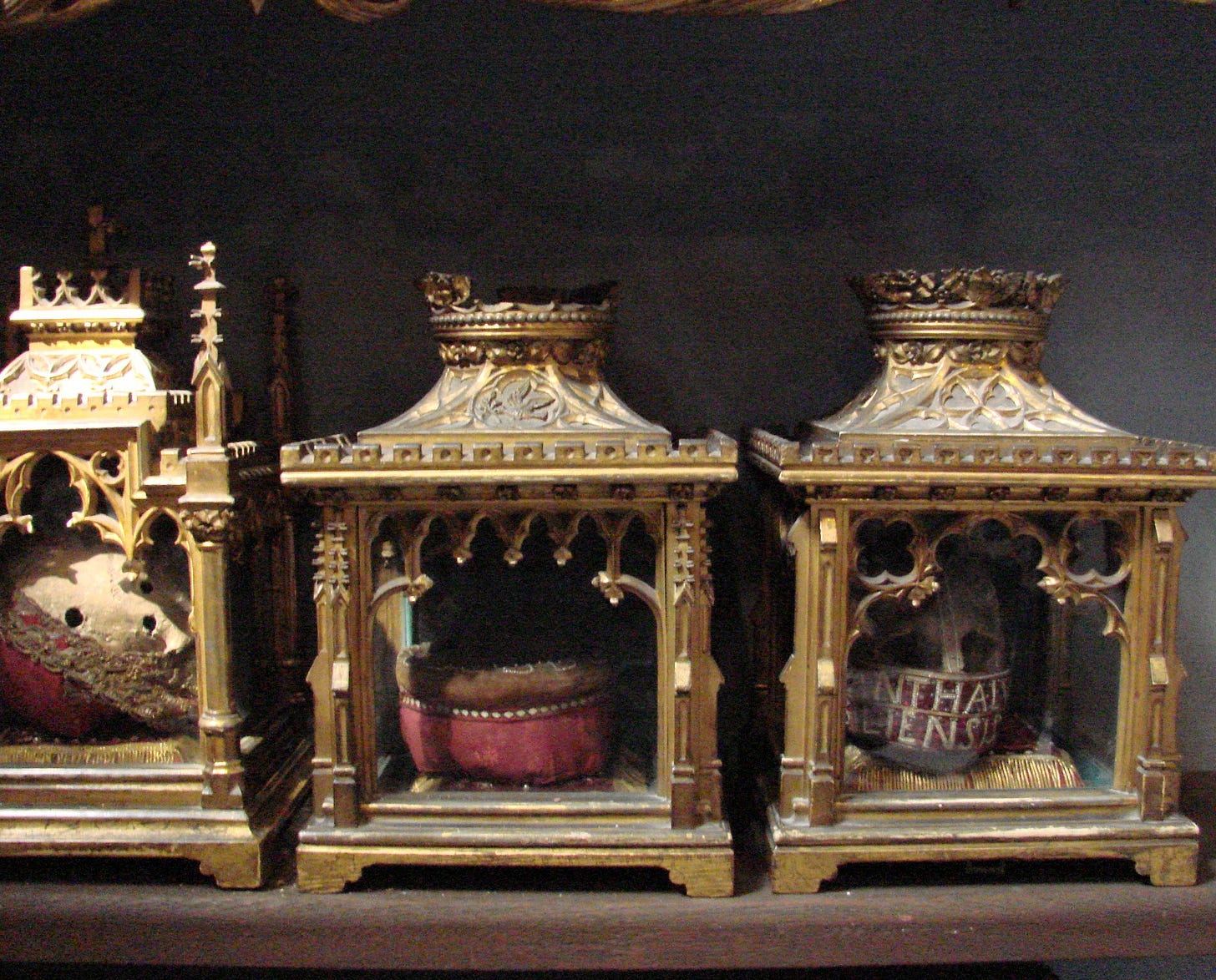 A photograph of elaborate glass boxes gilded with filigree. Inside each one is a skull, some with holes, all adorned with red velvet embroidered with Latin words