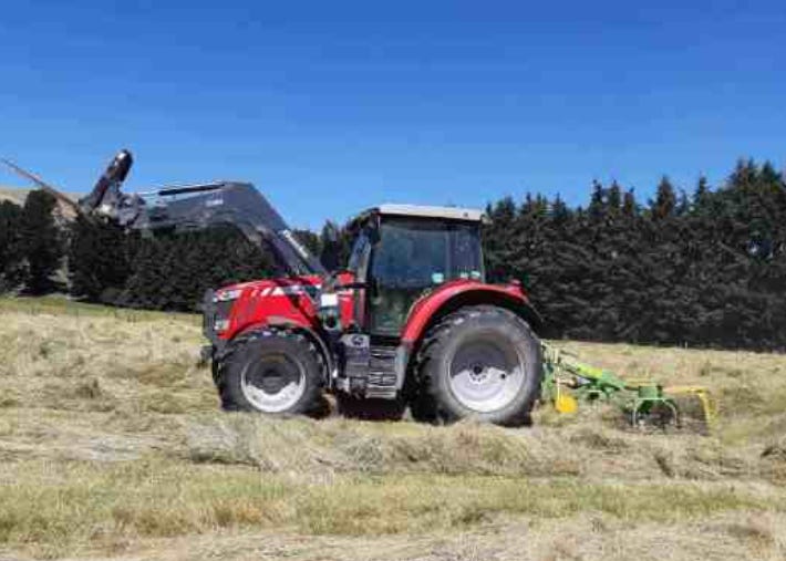 A red tractor towing a machine along rows of dried grass to fluff it up ready to be baled for hay. A red tractor towing a machine along rows of dried grass to fluff it up ready to be baled for hay.