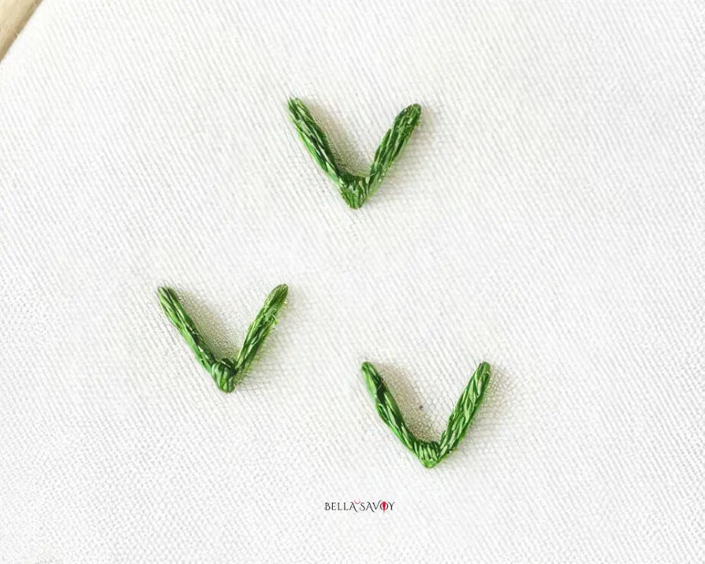 3 green fly stitches on white fabric