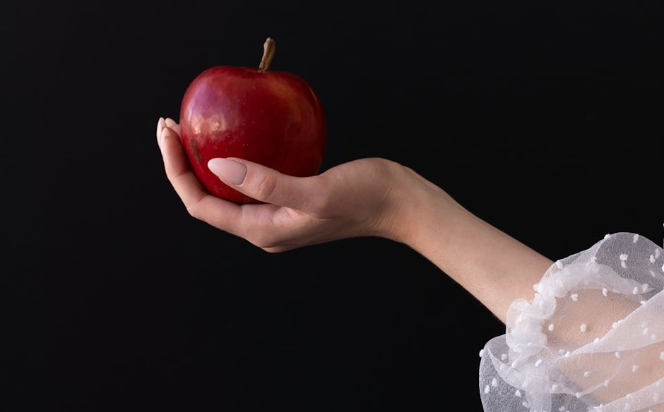 A woman in a white dress holding an apple