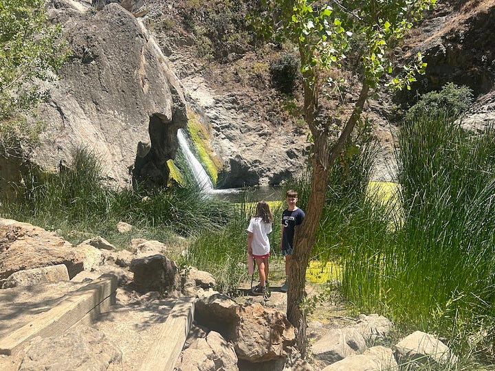Photos of a desert hike featuring pictures of brown landscape, a waterfall, the author, a teepee, and a fence post with a quote on it.