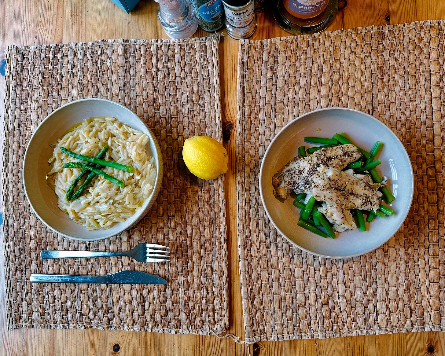 Top-down bowl of orzo with pan-fried fish and bright green vegetables; lemon and parmesan visible.