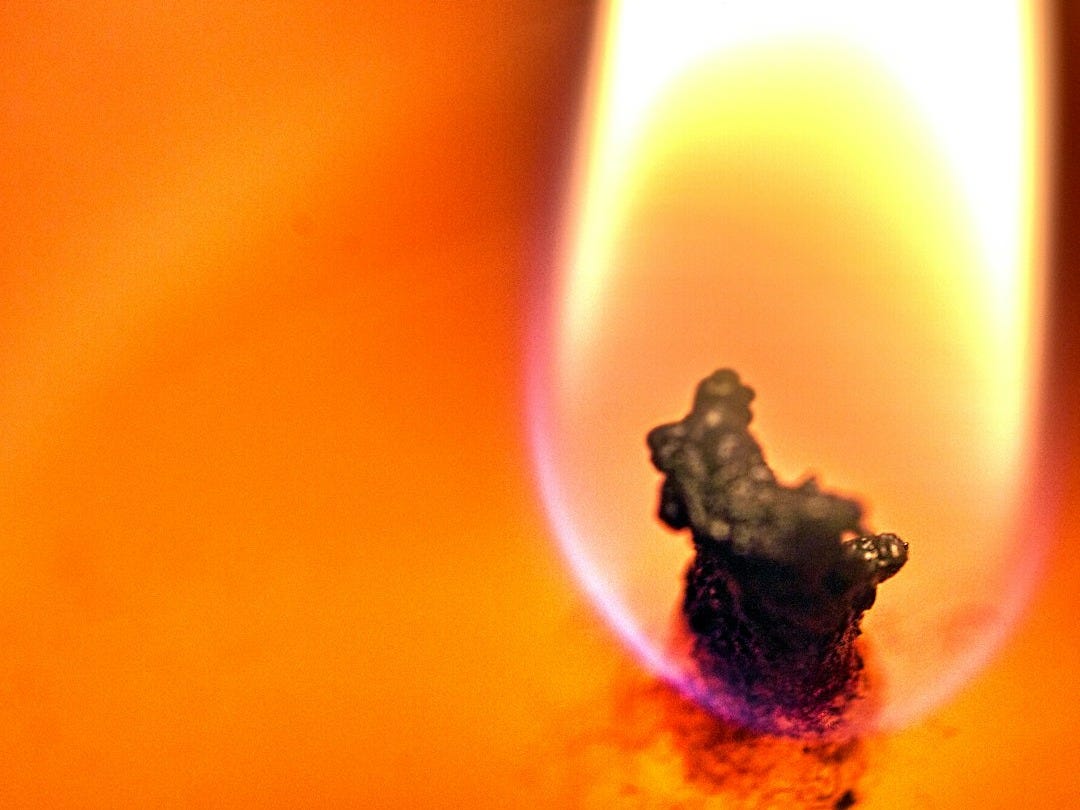 A lit candle with a small black object on top of it