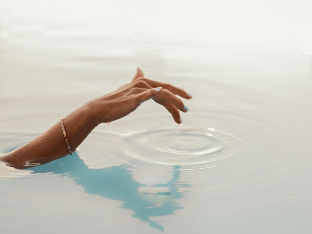 a person's hand reaching for something in the water
