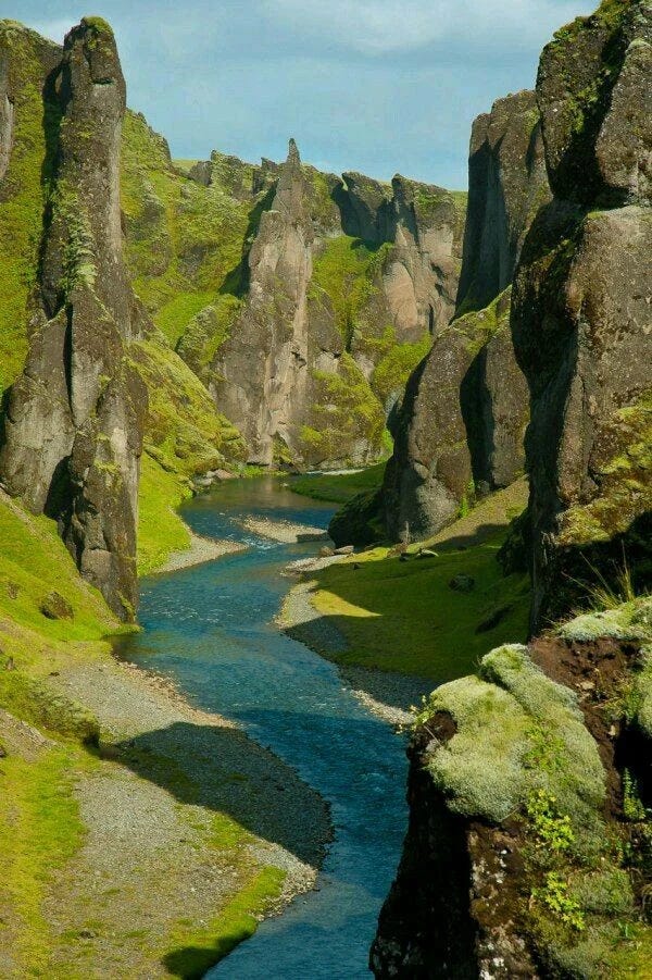 Dramatic moss-covered canyon with towering rock formations and a winding blue river flowing through its base.