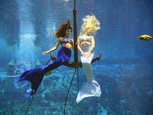 two mermaids sitting on a huge anchor under blue water