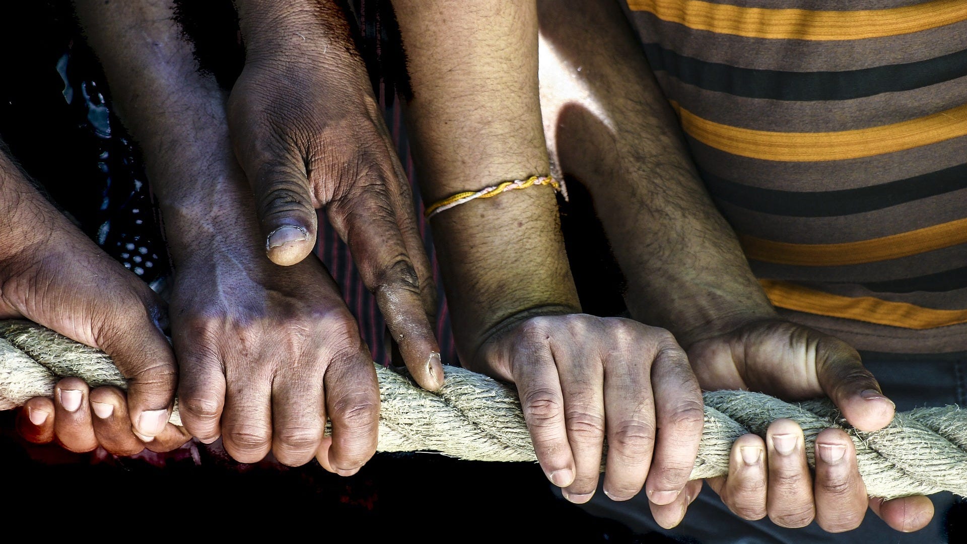 Photo of hands of several people, all holding a rope
