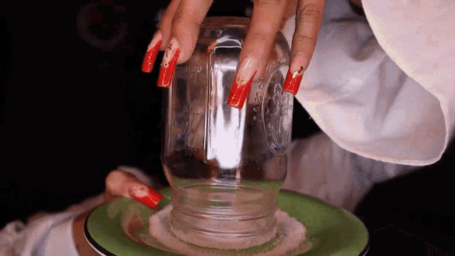 a woman with long red nails holds a mason jar on a plate