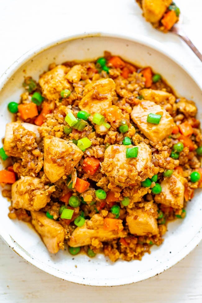 A bowl of cauliflower chicken fried rice topped with scallions. A bowl of cauliflower chicken fried rice topped with scallions.