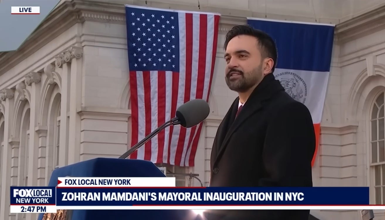Video screenshot of Zohran Mamdani in side view, speaking in front of New York City Hall, with US and New York state flags in the background. Video screenshot of Zohran Mamdani in side view, speaking in front of New York City Hall, with US and New York state flags in the background.