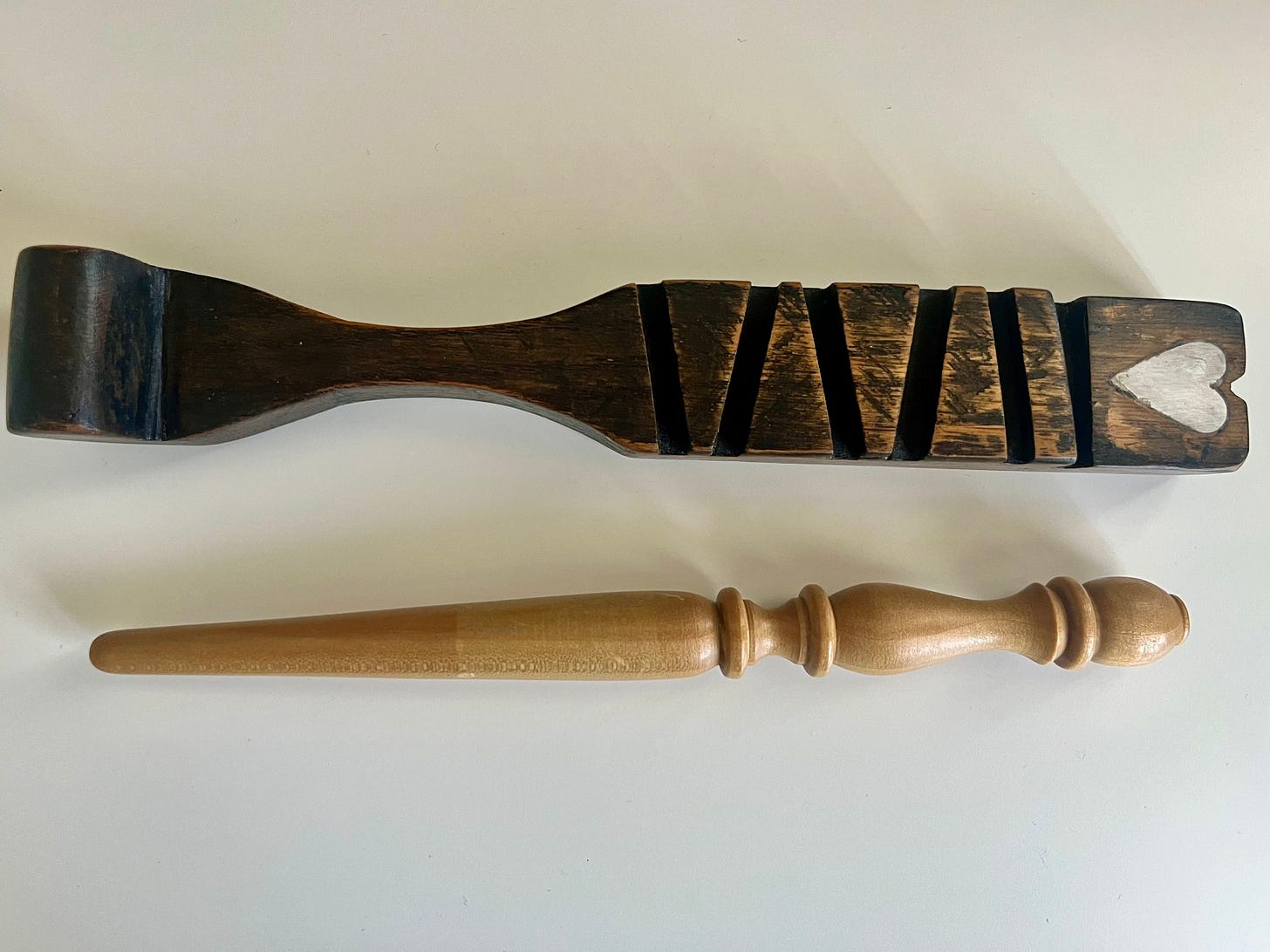 Antique carved wooden knitting sheath with a heart motif, beside a plain modern wooden sheath.
