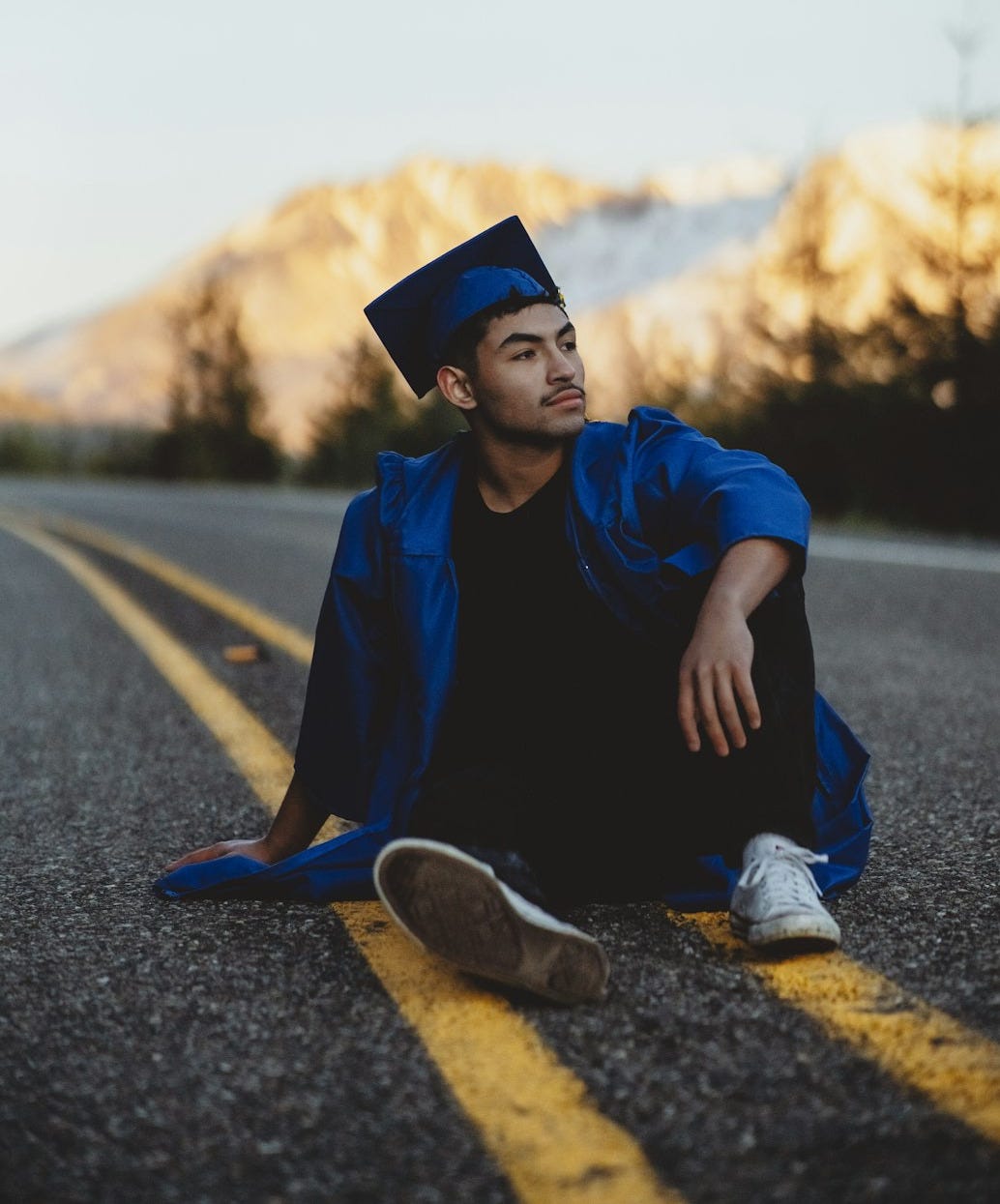 man in blue jacket and black pants sitting on road during daytime