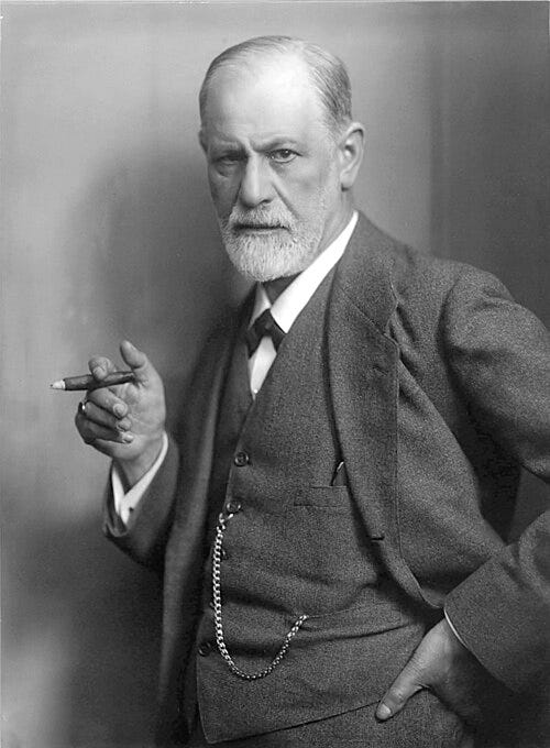 Old, black and white photo of Sigmund Freud, a middle-aged white man with white hair and a beard, holding a cigar, wearing a three-piece suit with a watch chain.