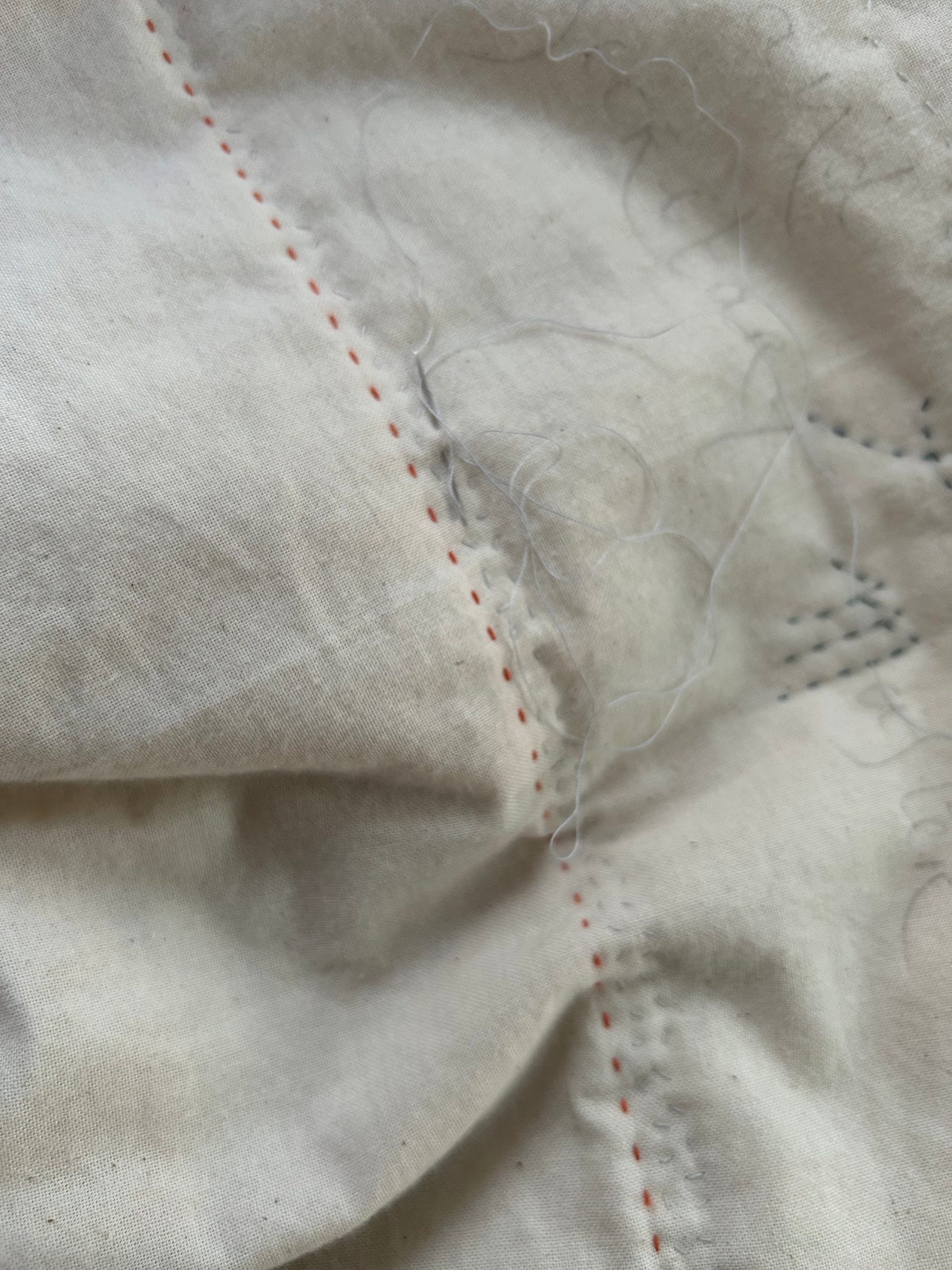 Stiching on cream calico, a needle and thread in the fabric.