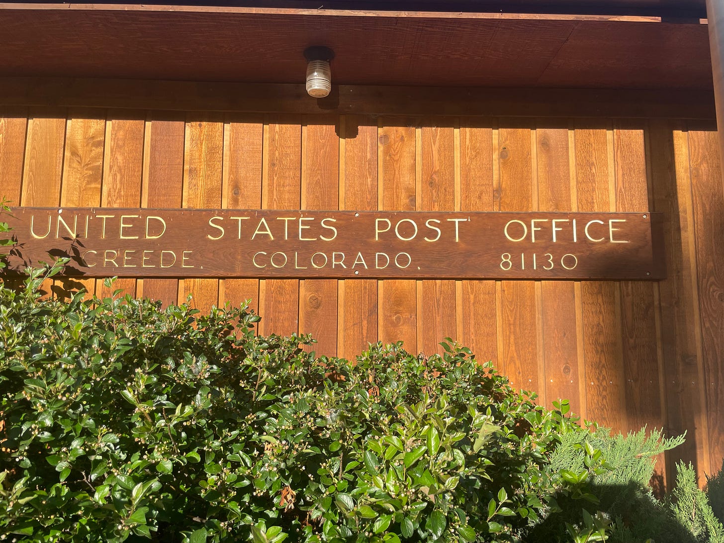 A close-up front exterior shot of the Creede, CO post office, which is vertically paneled in Cedar and features a sign that looks more like a ranger station than a post office.