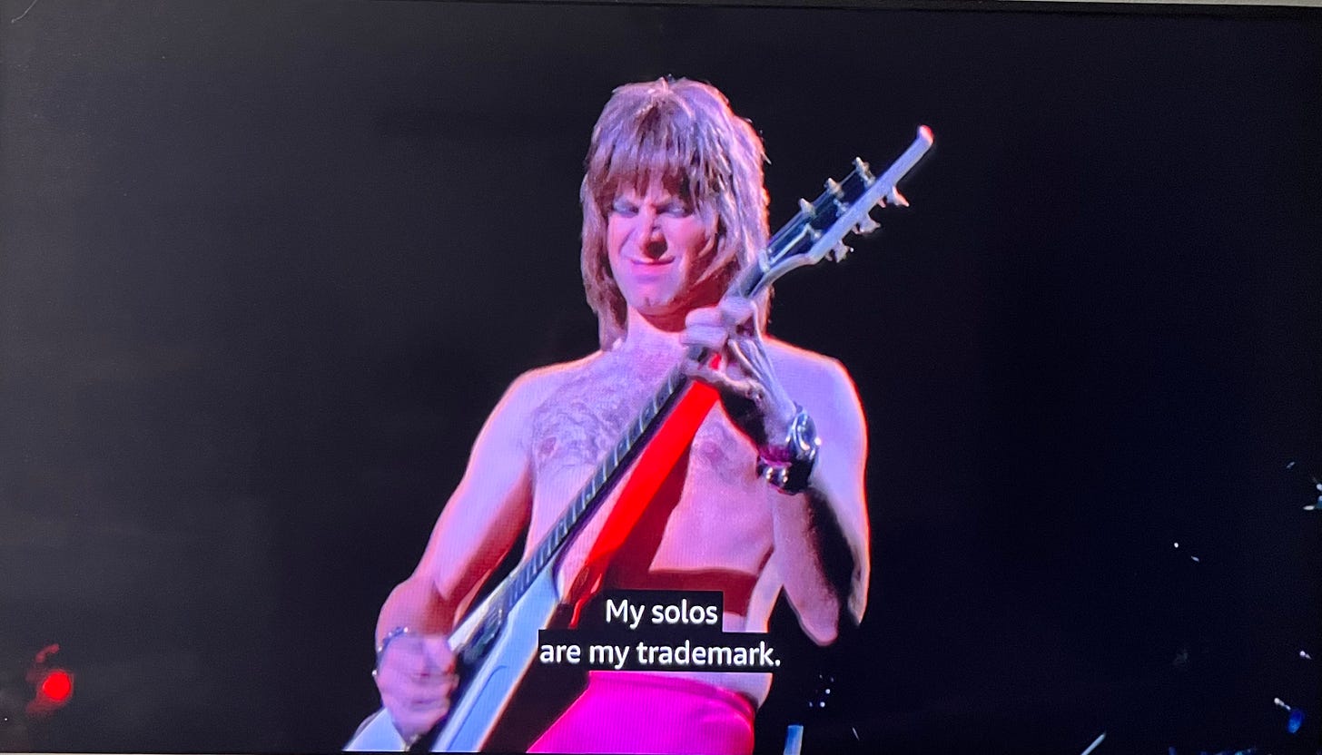 Image from This Is Spinal Tap: Nigel playing the guitar shirtless, and the voiceover narration is him saying, “My solos are my trademark.”