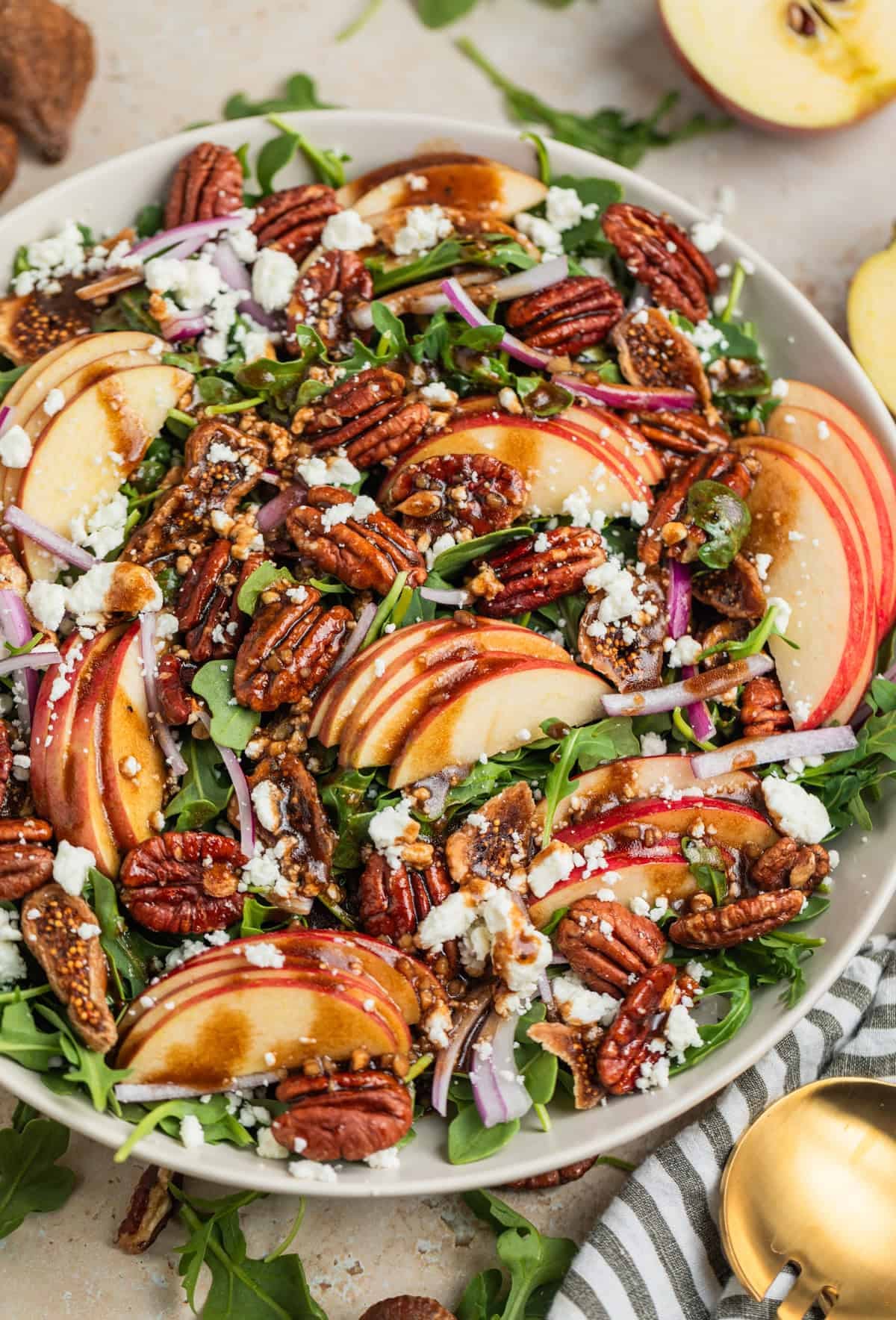 Salad bowl with arugula, sliced apples, goat cheese crumbles, onion and pecans topped with dressing.