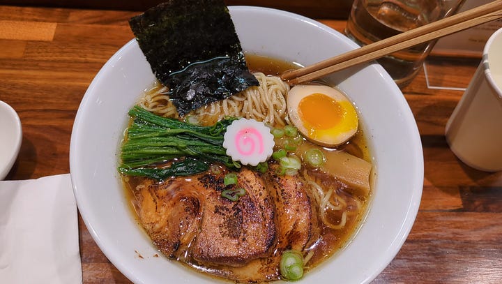 Shoyu Truffle Ramen bowl with pork chashu, and Spicy Negi Tonkotsu ramen with noodles being pulled up.