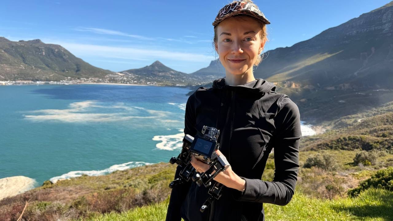 Olga at Chapman's Peak Drive on the Cape Peninsula, holding the small Ratel-1 robot up above the Atlantic Ocean. Sentinel mountain visible behind.