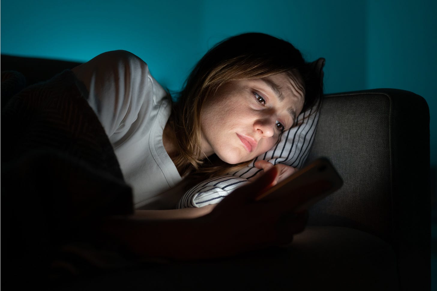 Woman lying on sofa at night scrolling on her phone
