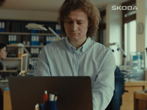 a man sitting in front of a laptop with skoda written on the wall behind him