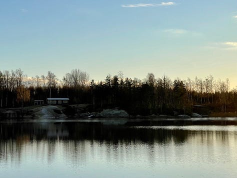 Differing angles of blue sky and water in winter, with some some rocks, houses, wintery trees and sun