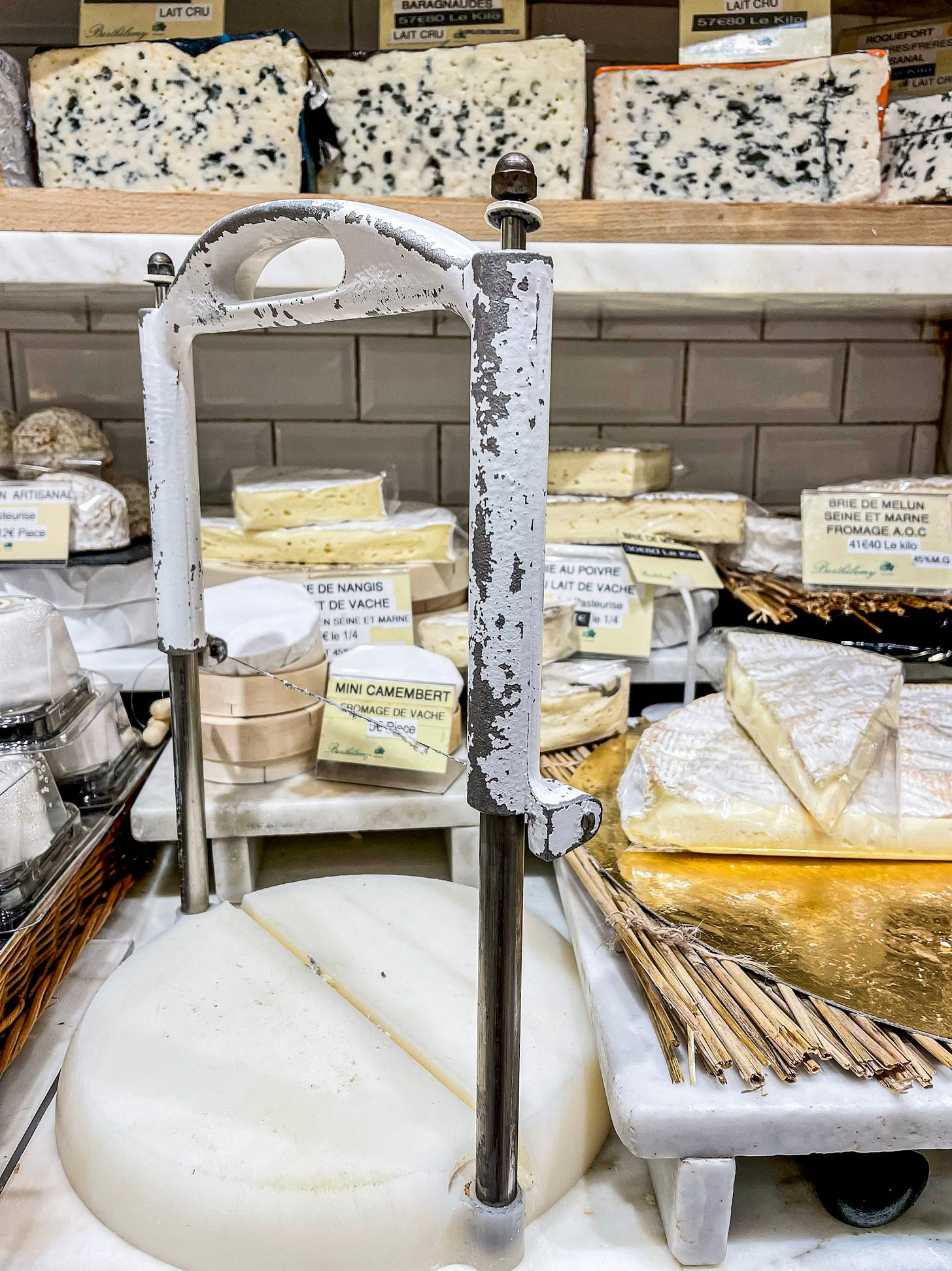 Traditional French cheeses displayed behind a vintage cheese cutter inside Barthélémy, one of Paris's most celebrated fromageries. Traditional French cheeses displayed behind a vintage cheese cutter inside Barthélémy, one of Paris's most celebrated fromageries.