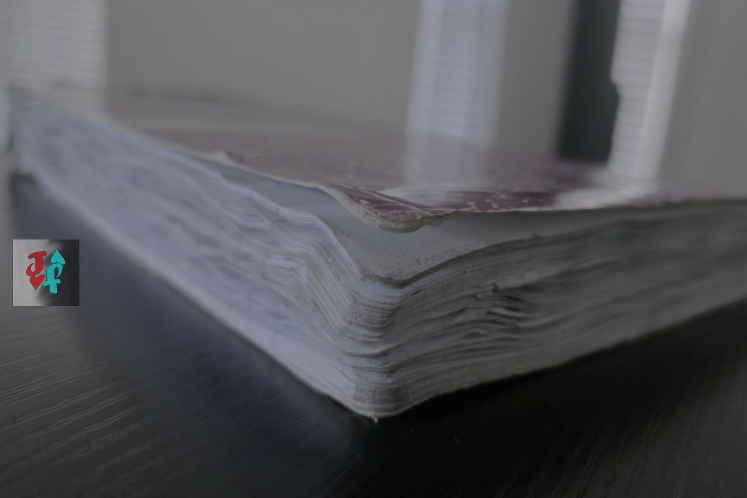 A photo of an old, used notebook sitting on a black desktop in a room lit by afternoon sunlight.