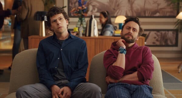 Two men, seated on chairs in a lobby-type area, looking thoughtful. 