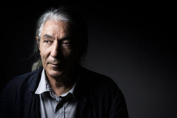 A man posing for a photograph against a dark background.