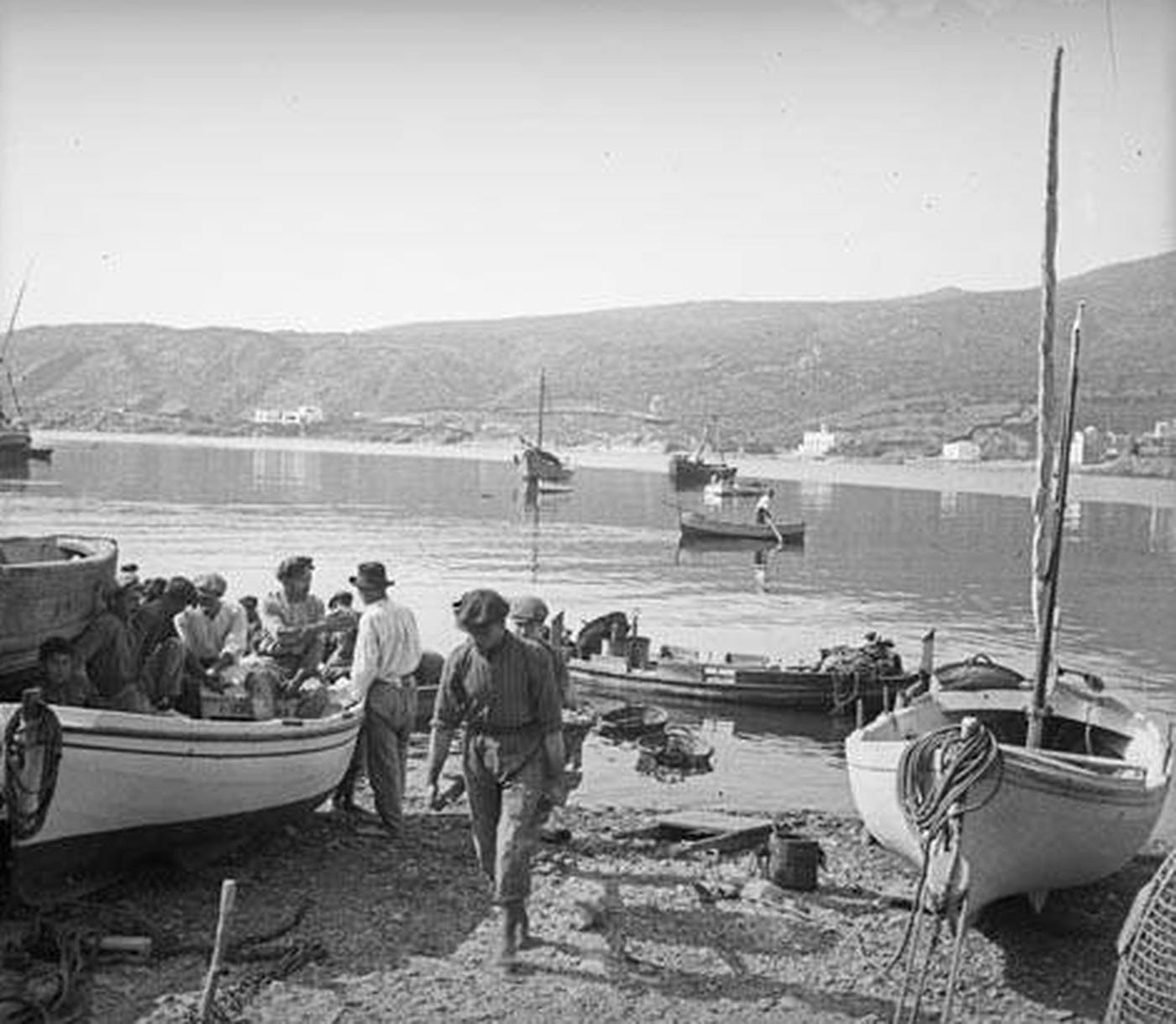 Men standing around wooden boats hauled up on the beach at Cadaqués, the bay behind them. Men standing around wooden boats hauled up on the beach at Cadaqués, the bay behind them.