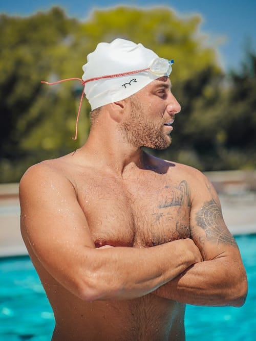 Free Shirtless tattooed man with swimming cap at the poolside, looking focused and ready. Stock Photo