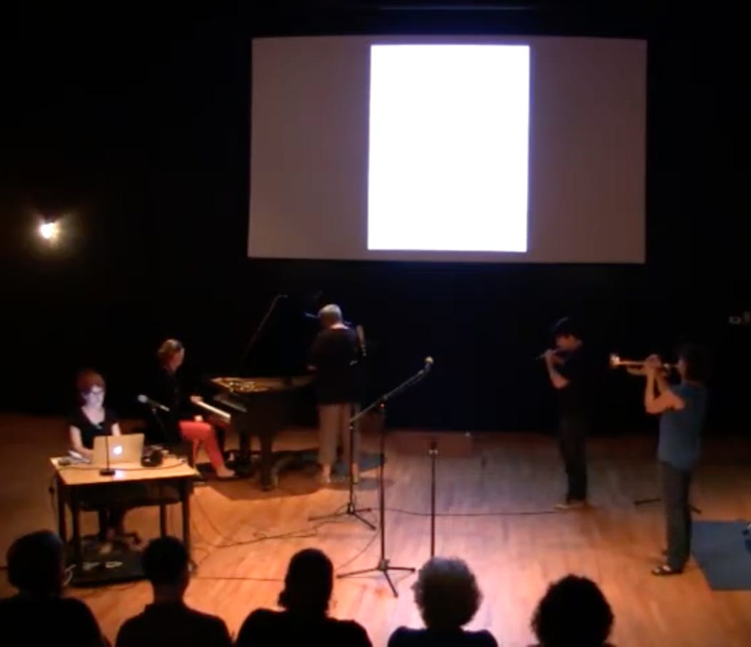 Stage with poet at a desk, projection screen behind, and musicians onstage too