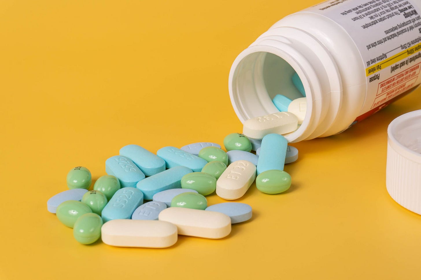 Photo by Etatics Inc. on Pexels Open bottle of assorted pills spilling onto a vibrant yellow background. (stock photo)