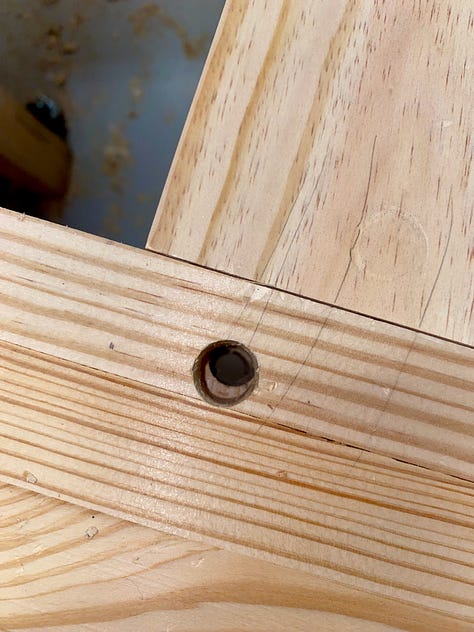 Holes bring drilled, via a drill press, into the bench legs; overlapping drawbore holes; sanding drawbore pegs; and then waxing and temporarily inserting them into the bench base.