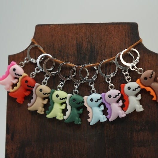 May include: A set of ten colorful dinosaur keychains. Each keychain features a different color dinosaur with a silver key ring. The keychains are displayed on a wooden stand.