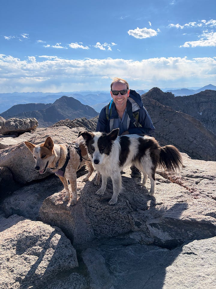 a woman, man and two dogs in front of the Mount Blue Sky sign and two dogs and a man on top of Mount Blue Sky