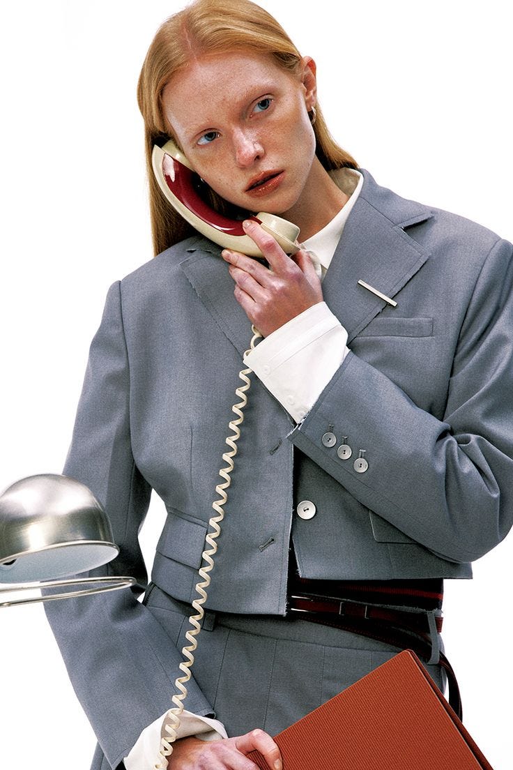 This may contain: a woman in business attire is talking on the phone and holding a binder over her shoulder