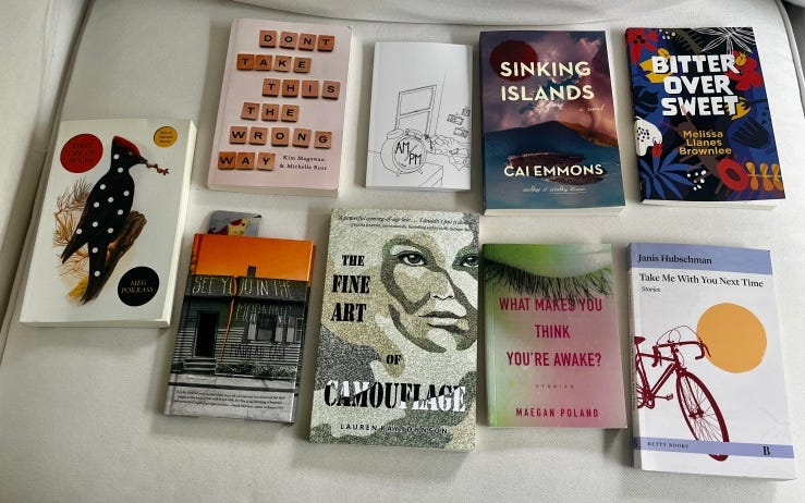 Nine books produced by small presses are laid out on a white sofa. First Law of Holes by Meg Pokrass, Don't Take This the Wrong Way by Kim Magowan & Michelle Ross, AM/PM by Amelia Gray, Sinking Islands by the late Cai Emmons, Bitter Over Sweet by Melissa Llanes Brownlee, See You in the Morning by Mairead Case, The Fine Art of Camouflage by Lauren Kay Johnson, What Makes You think You're Awake? by Megan Poland, and Take Me with you next Time by Janis Hubschman.