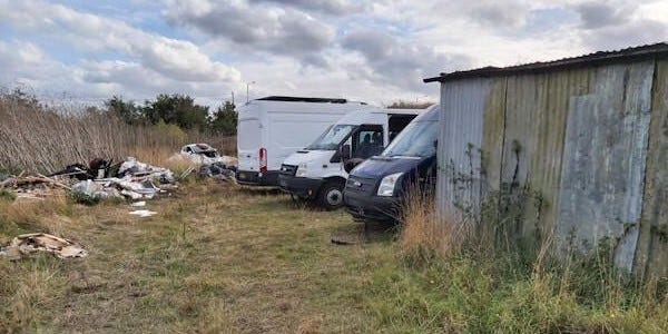 grassy area behind outbuilding with three vans parked
