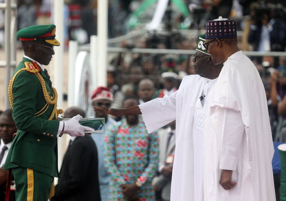 Two men in white native attire facing a man in full ceremonial military uniform. Two men in white native attire facing a man in full ceremonial military uniform.