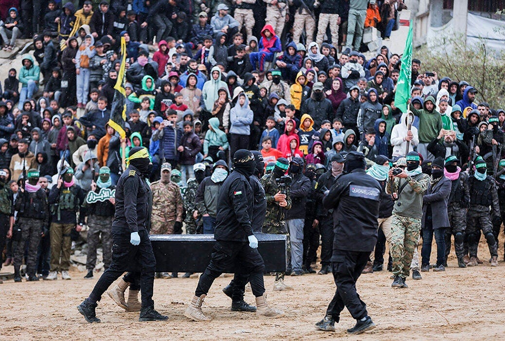 Picture shows Hamas militants taking pictures as fellow masked Palestinian fighters carry one of the coffins during the handover of the bodies of four Israeli hostages to the Red Cross in Khan Yunis