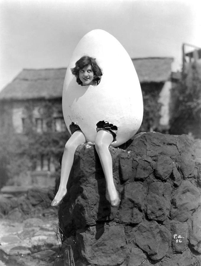 This may contain: a woman sitting on top of a rock with an egg in the shape of a person