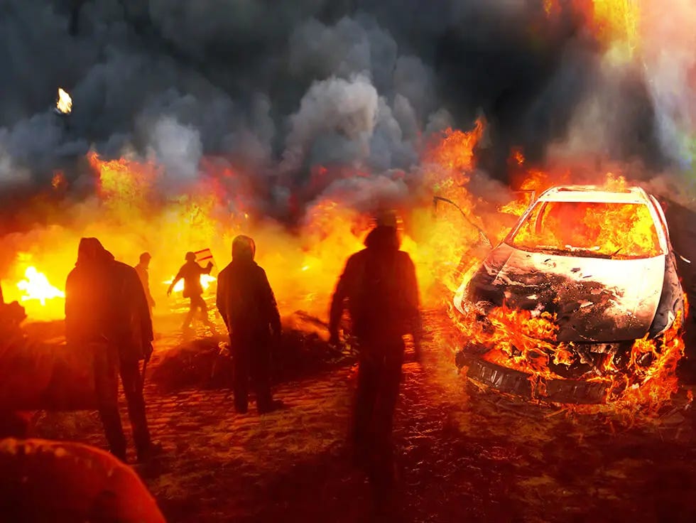 Individuals near a vehicle on fire with smoke in the background Individuals near a vehicle on fire with smoke in the background