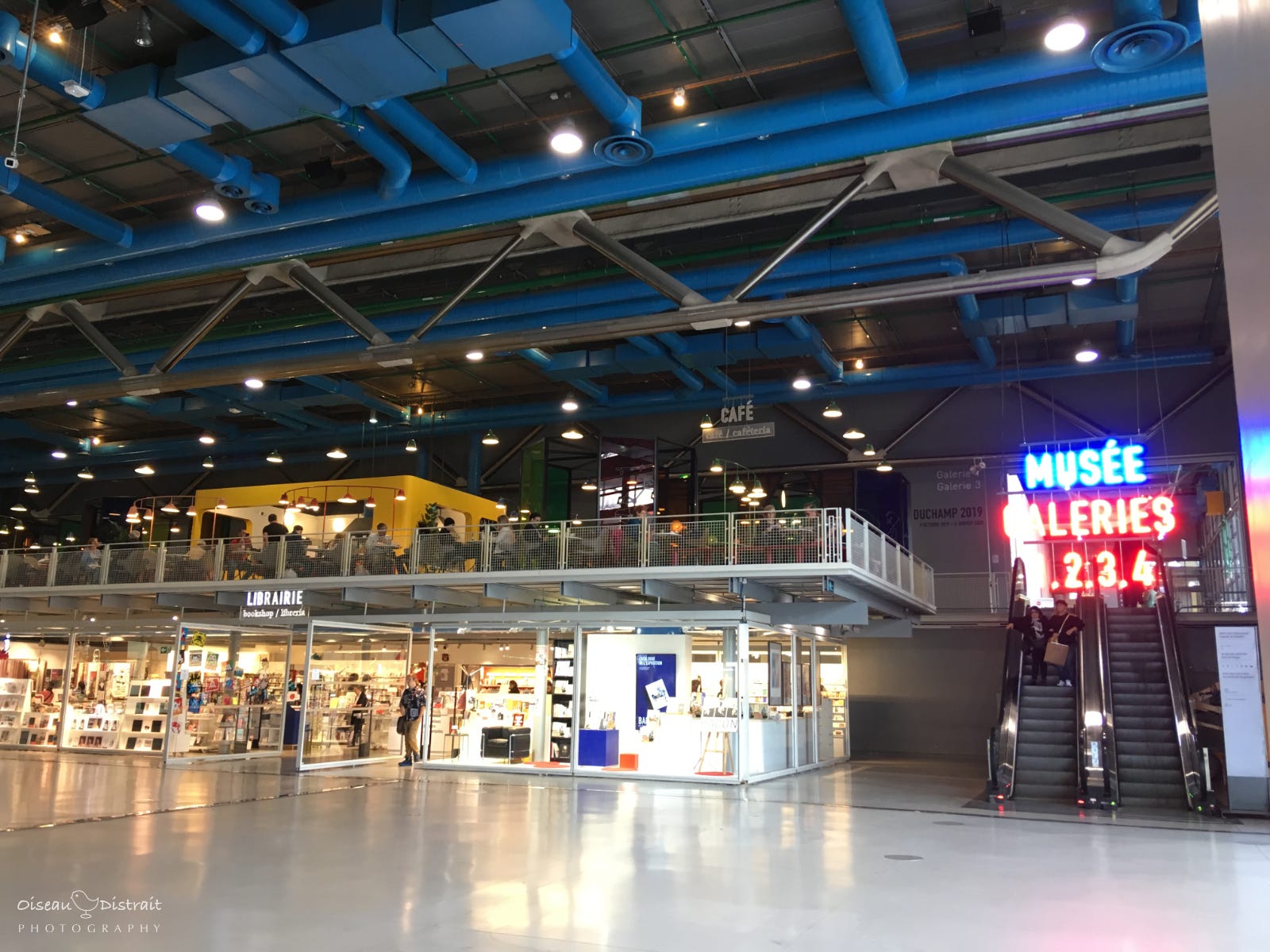 Interior of Centre Pompidou in Paris. Blue metal ceiling of M&E structure, and far end with neon light signage. Interior of Centre Pompidou in Paris. Blue metal ceiling of M&E structure, and far end with neon light signage.