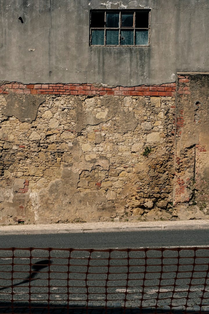 Streets of Lisbon. The faded grey coating on the wall has fallen on the ground floor. Red bricks can been seen among an assembly of yellow stones.